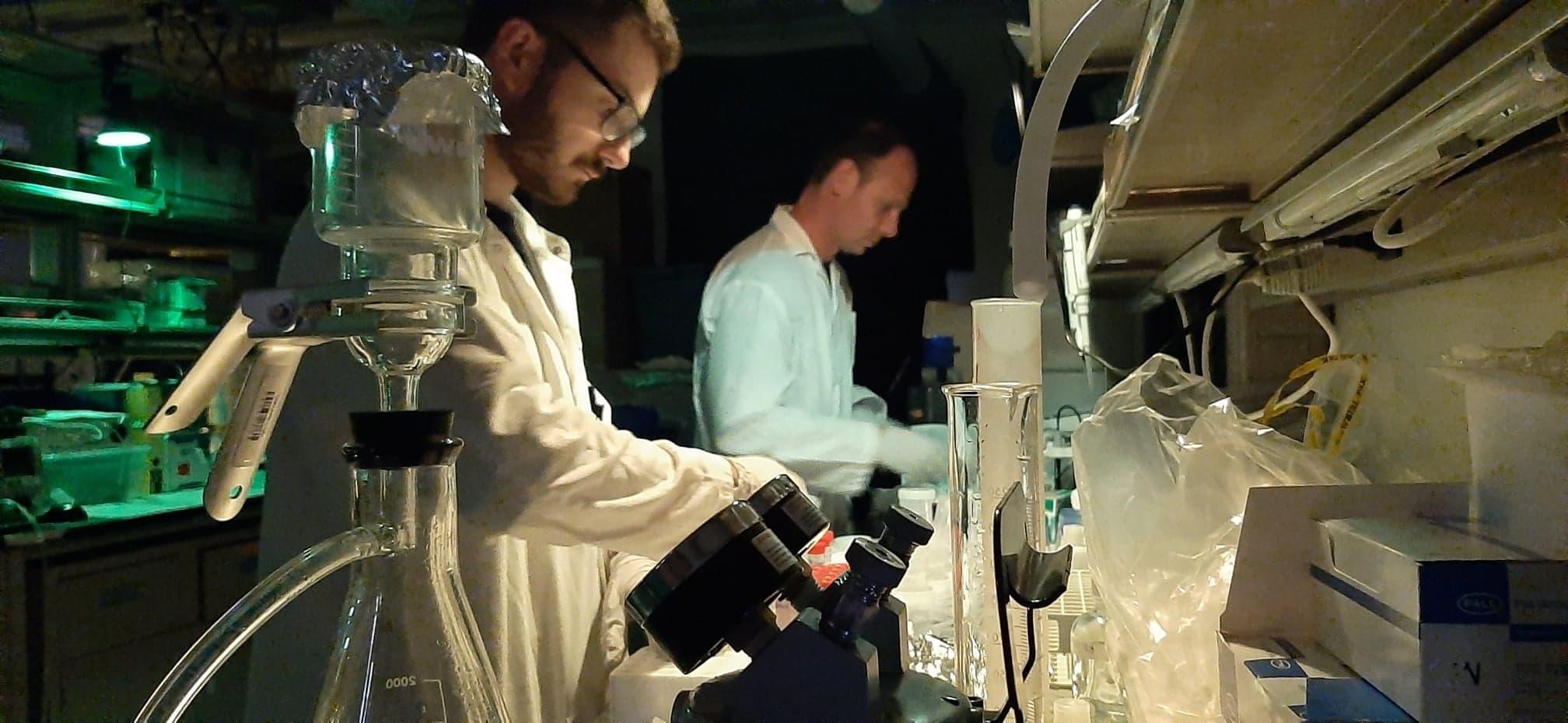 Lucas Tisserand (foreground) and Emmanuel Devred (background) processing water samples in the biogeochemistry lab at the Aurora Research Institute. Only green lighting is used in the lab as this wavelength is absorbed by plankton and therefore stops any photosynthesis processes that would change the conditions from when the sample was collected. ©Joannie Ferland. Takuvik2019 Picture9 9